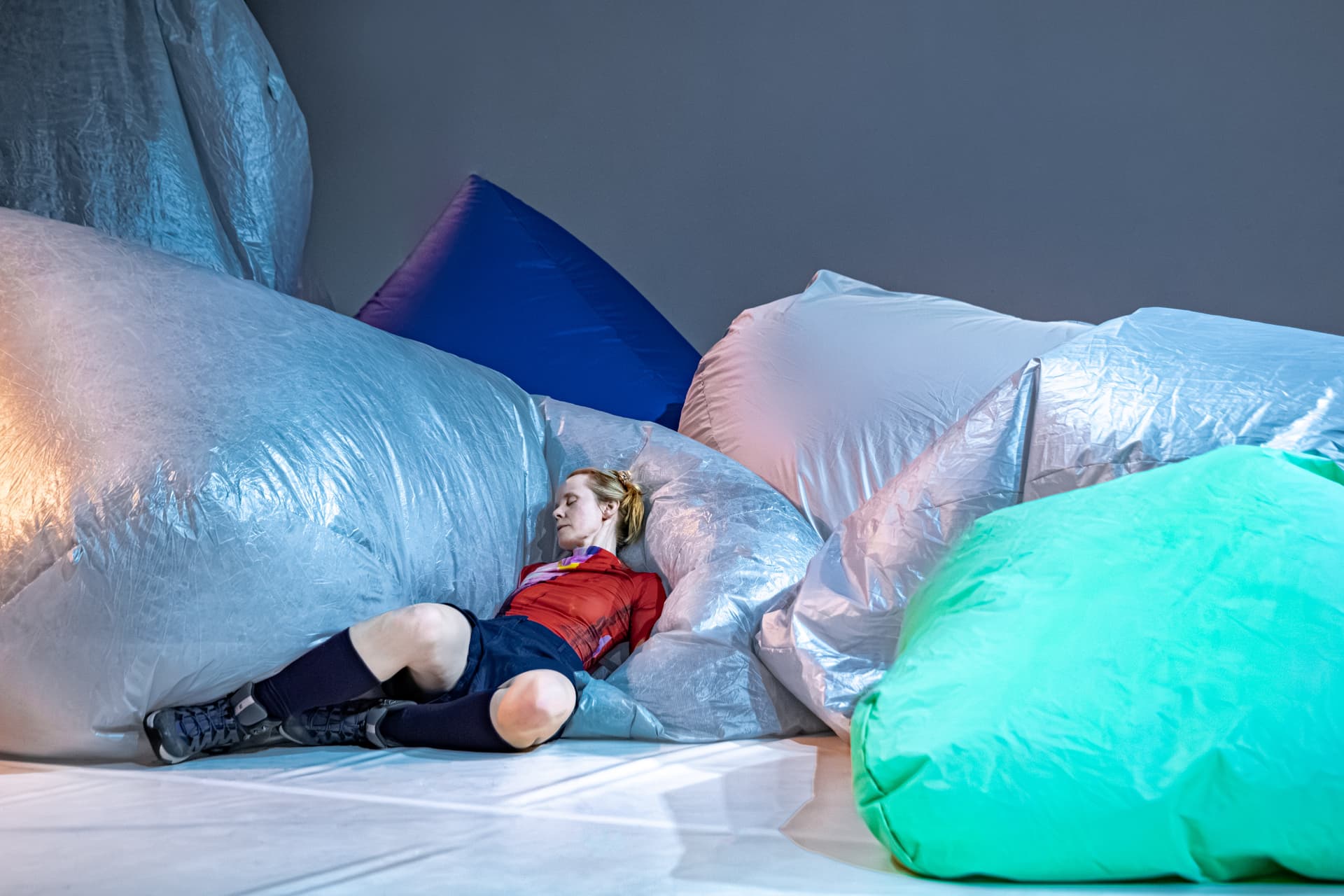 Performer resting among silver and turquoise inflatable forms