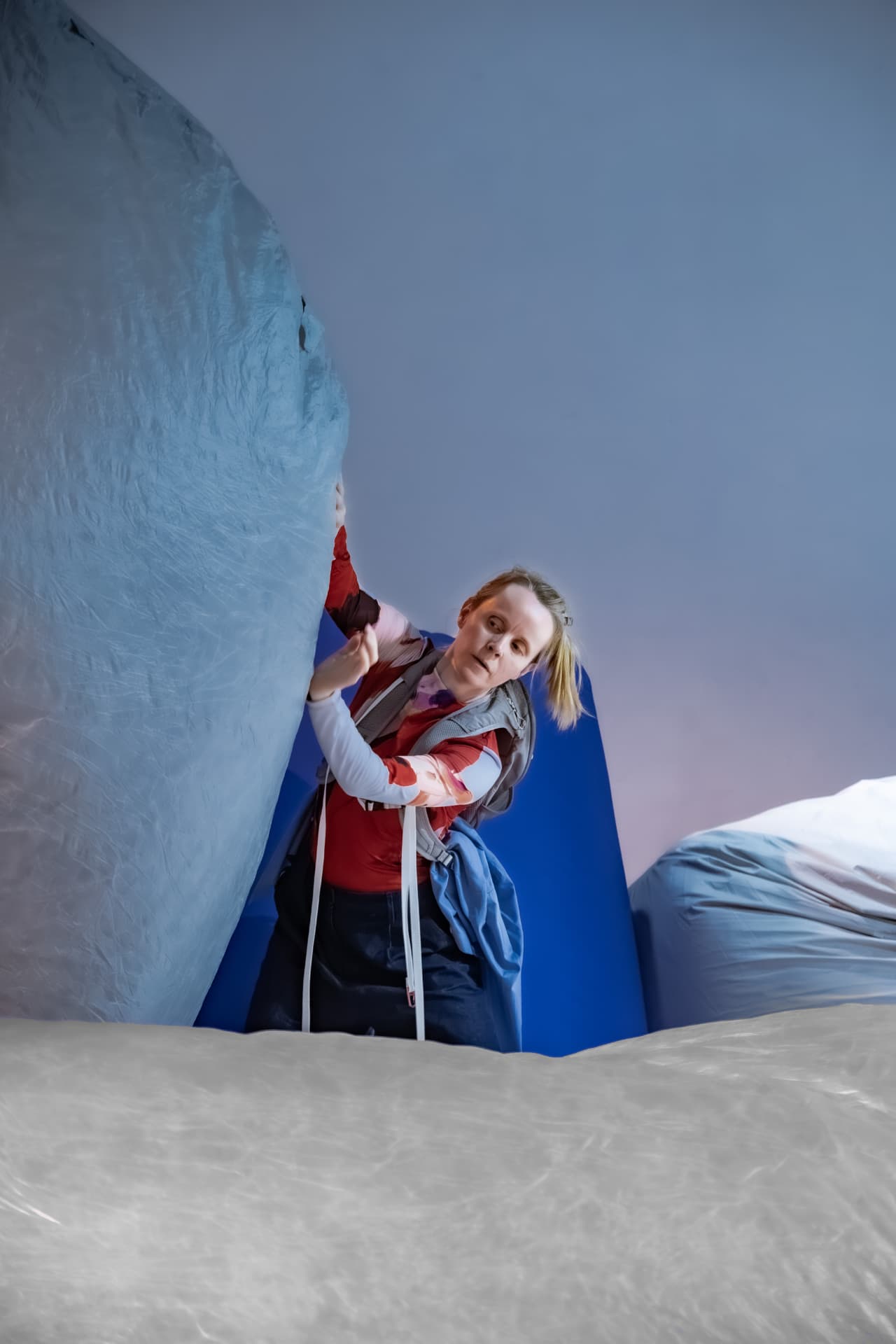 Performer leaning against an inflatable form in a blue artificial landscape